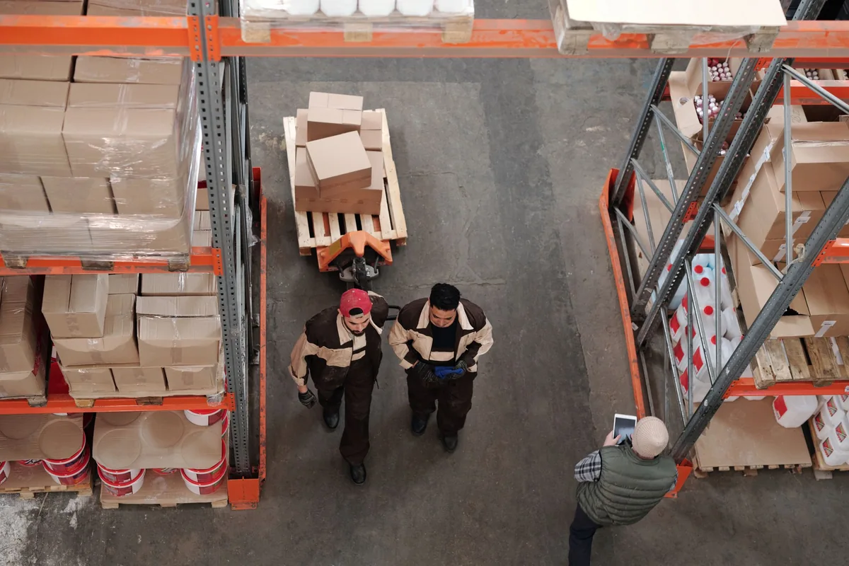 Overhead view of workers beside a pallet of boxes and warehouse shelving.