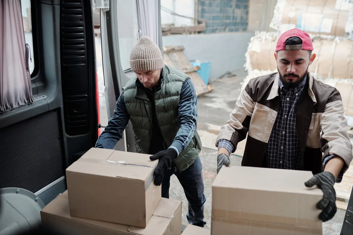 Two workers transferring cardboard boxes at the open rear of a delivery van.