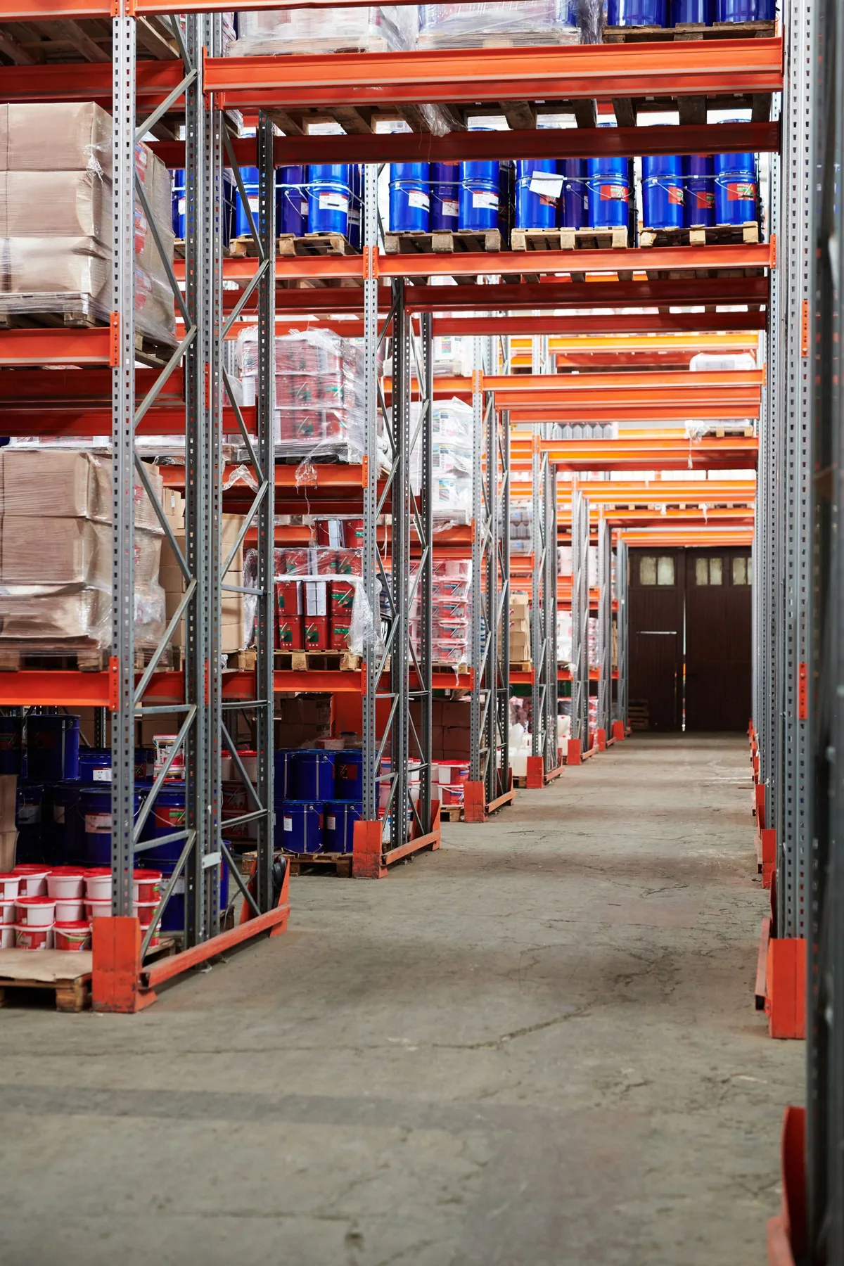 Warehouse aisle with pallets and packaged goods stored on metal racks.